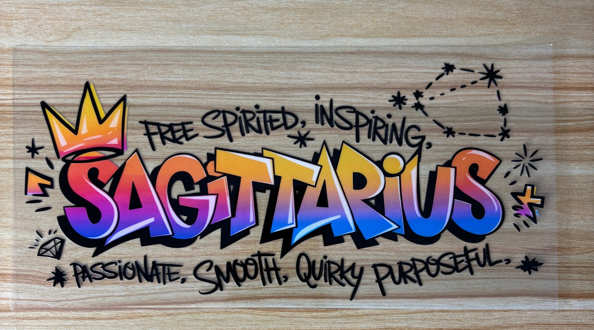 a colorful graffiti-style text that reads "Sagittarius" with a crown and stars surrounding it. The text is accompanied by the phrases "Free Spirited, Inspiring, Passionate, Smooth, Quirky Purposeful" in a stylized font.
