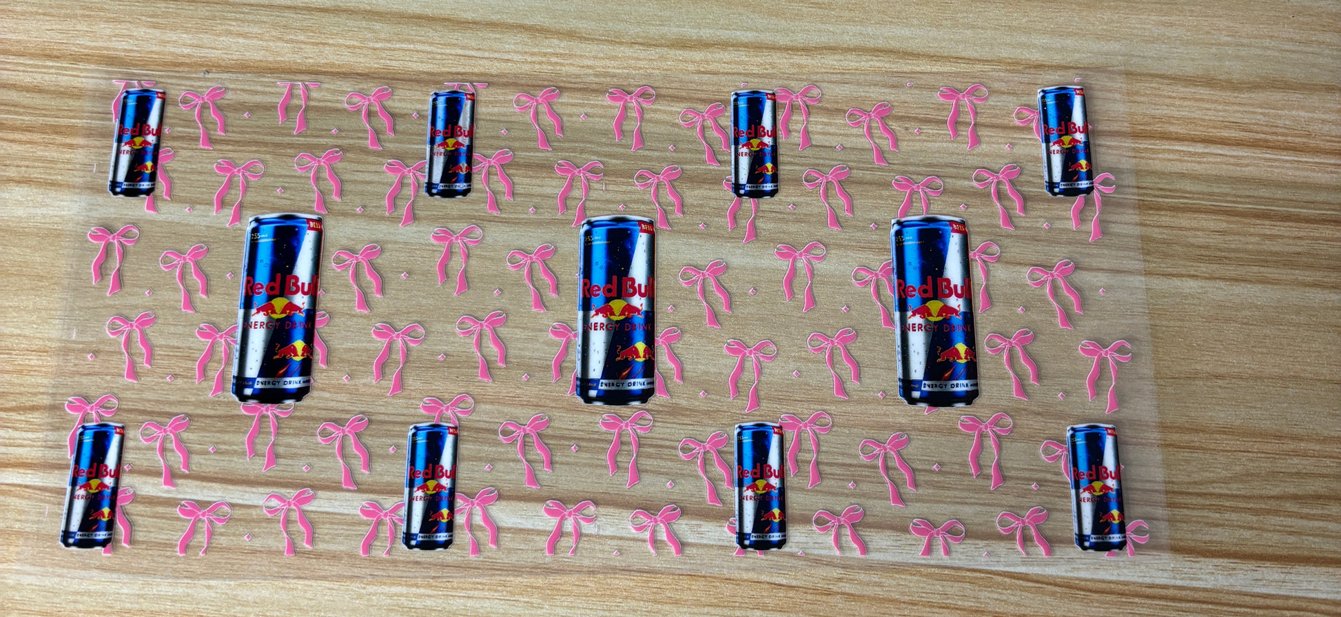 a pattern of red bull cans with pink bows scattered across a wooden surface.