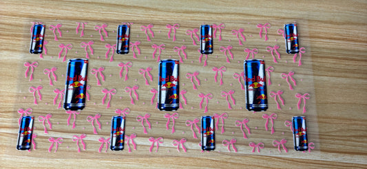 a pattern of red bull cans with pink bows scattered across a wooden surface.