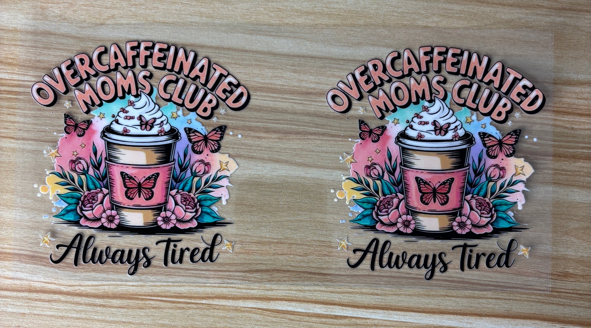 two identical illustrations of a coffee cup with a whipped cream topping, surrounded by flowers and butterflies. The text above the illustrations reads "Overcaffeinated Moms Club" and below it says "Always Tired".