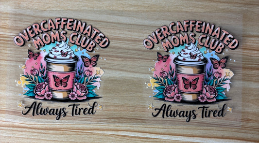 two identical illustrations of a coffee cup with a whipped cream topping, surrounded by flowers and butterflies. The text above the illustrations reads "Overcaffeinated Moms Club" and below it says "Always Tired".