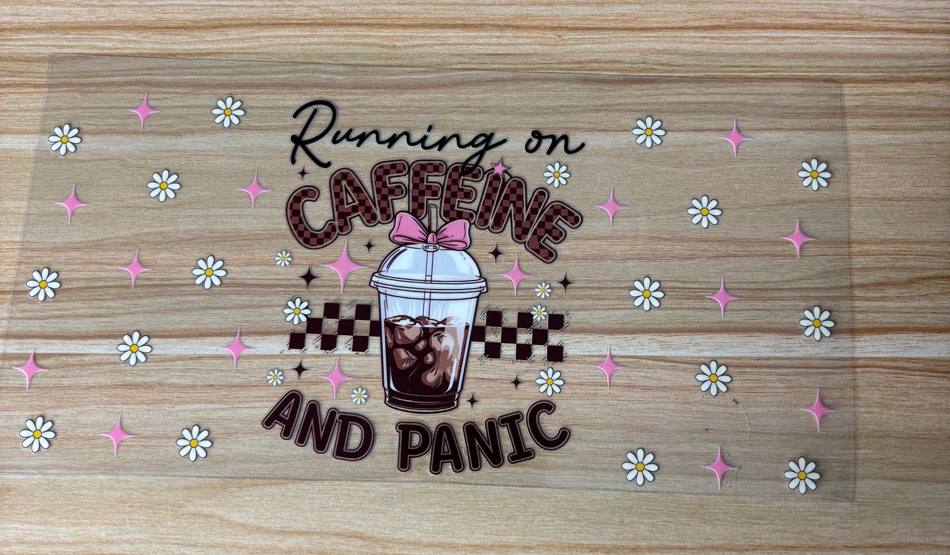A transparent object with a design featuring a cup of coffee and the text "Running on Caffeine and Panic" surrounded by pink and white flowers.