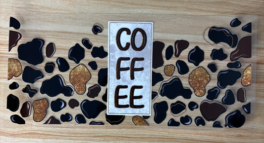 a coffee cup design with a central text label that reads "COFFEE". The design includes various shades of brown and black spots, resembling coffee stains or splatters, and gold glitter accents.