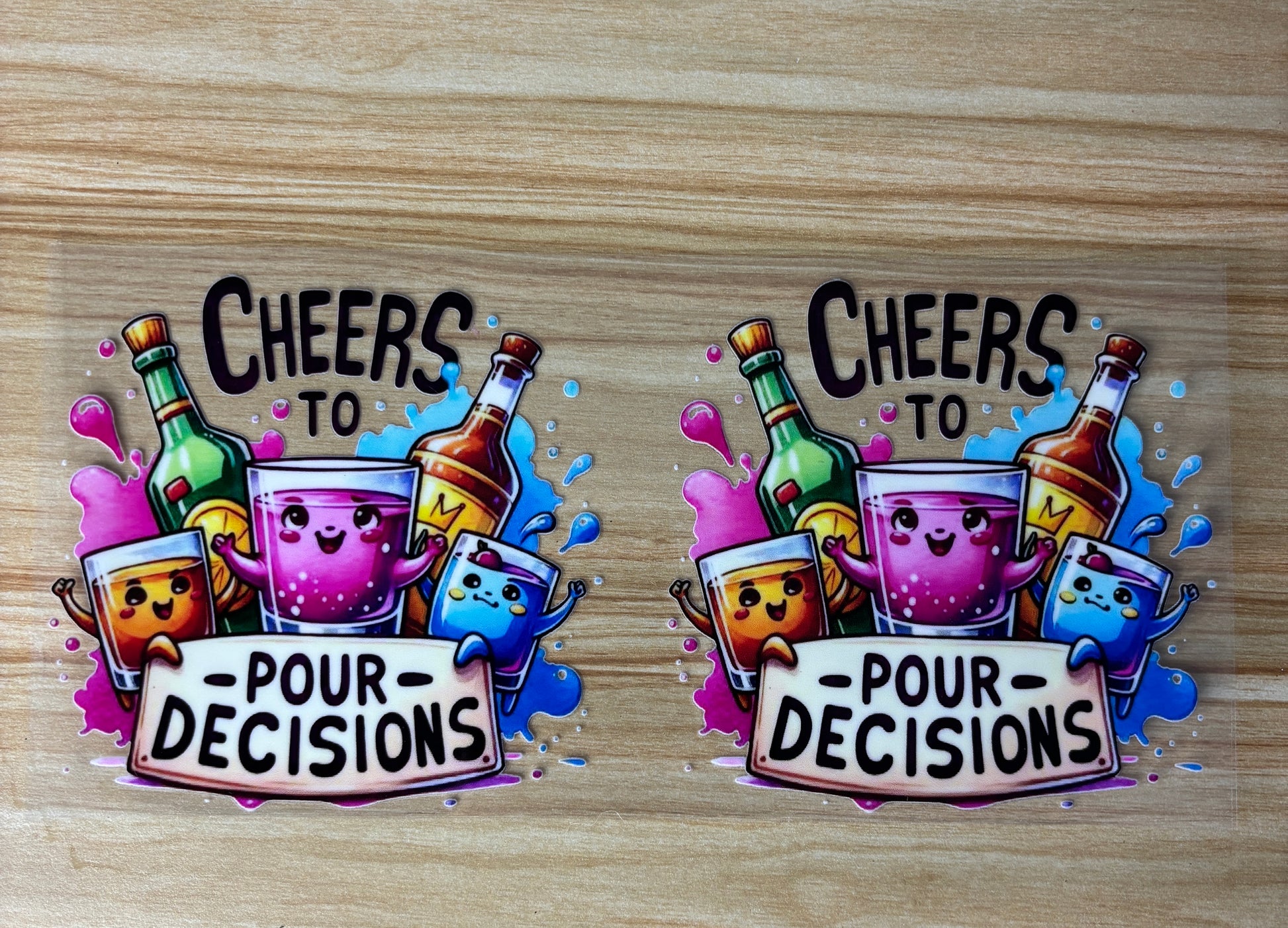 two stickers with a cheerful and colorful design, featuring cartoon-style characters and text. The stickers are placed on a wooden surface.